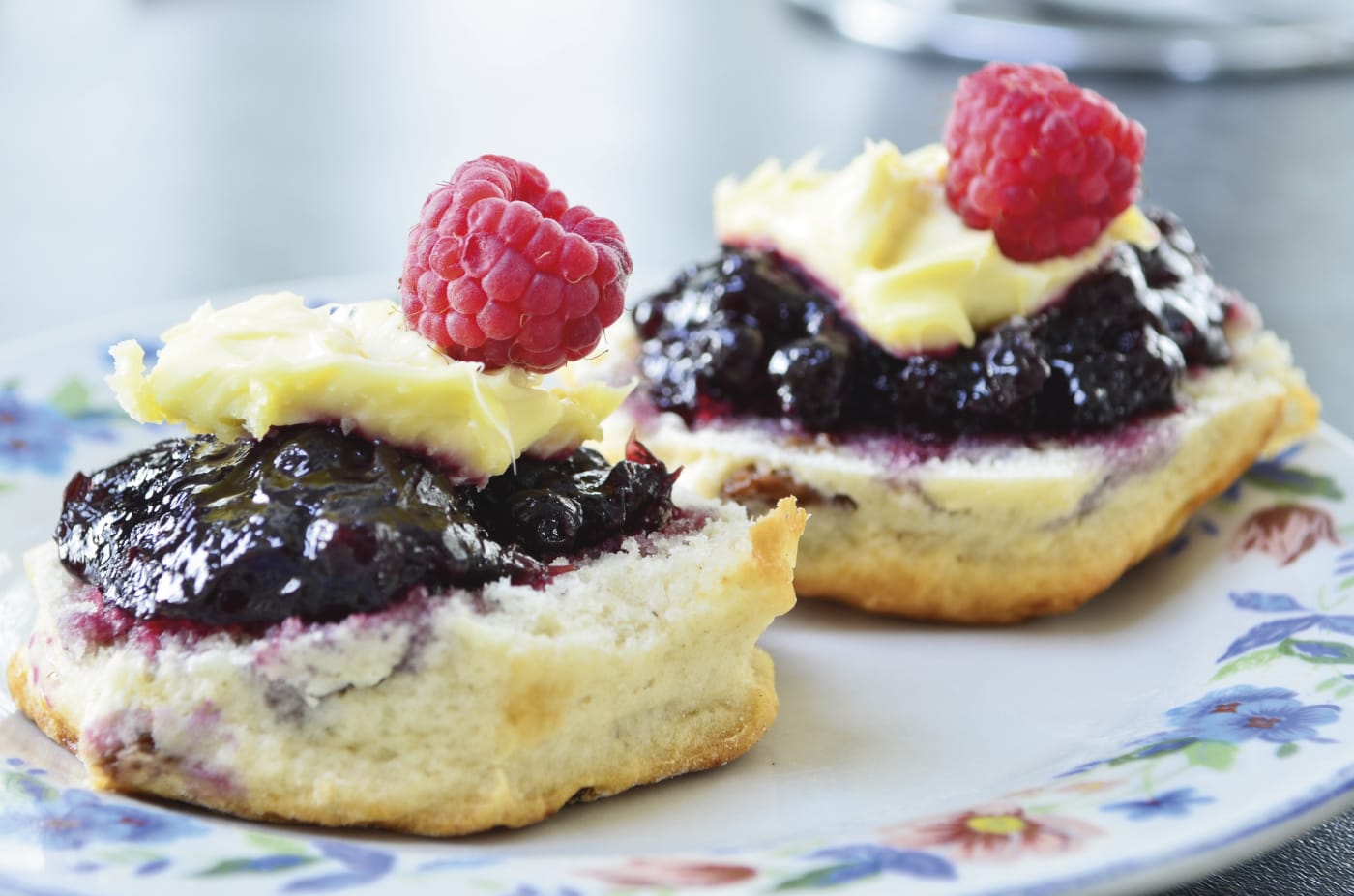 Two scones with jam and raspberry on top 