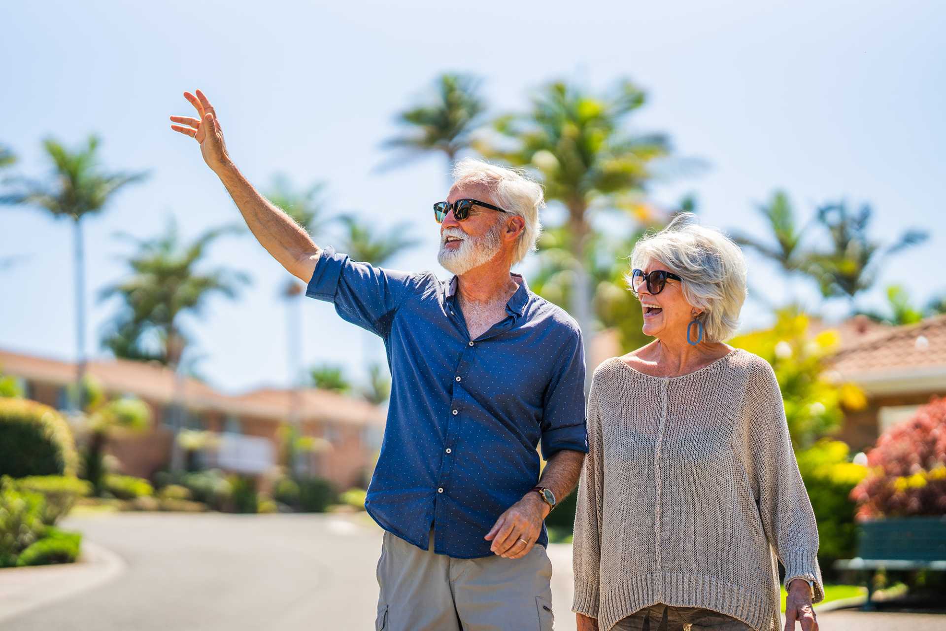 Happy retired couple waving to their neighbours in a retirement village.